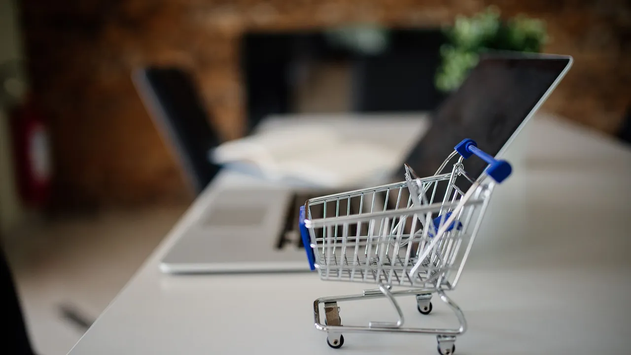 Mini shopping cart placed on a table next to a laptop in a modern office setting