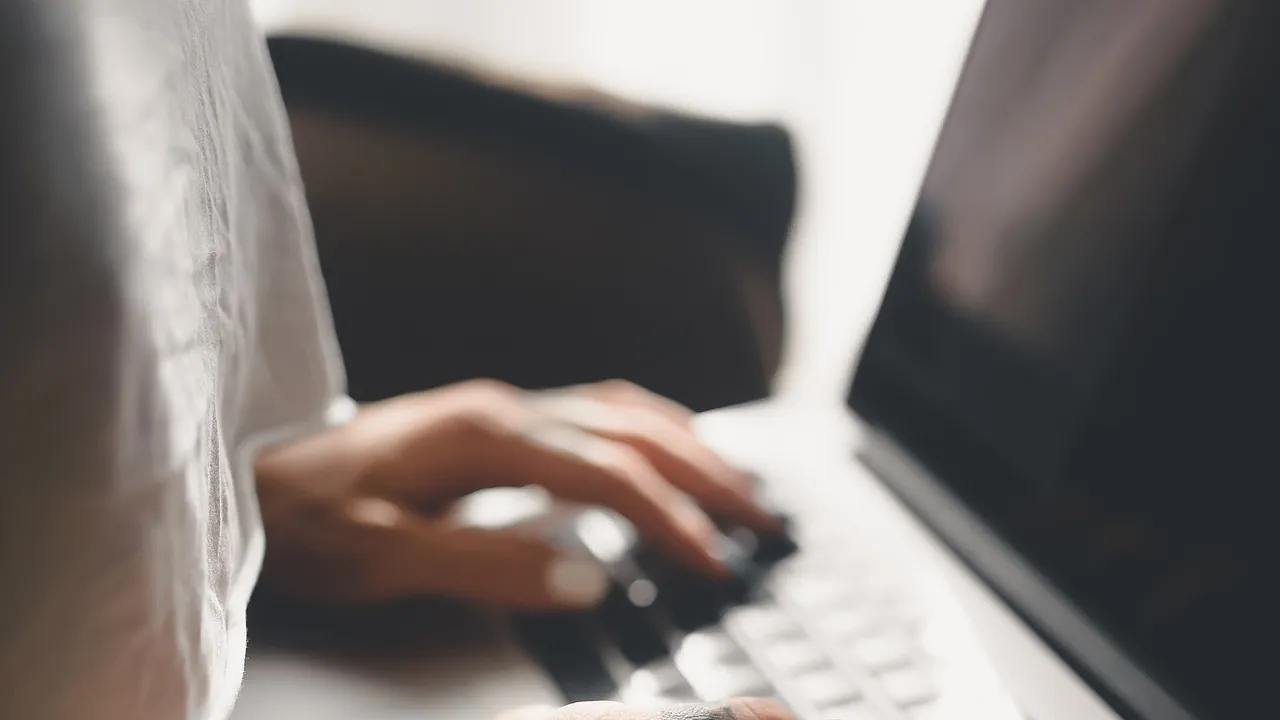 Hands are seen typing on a laptop keyboard