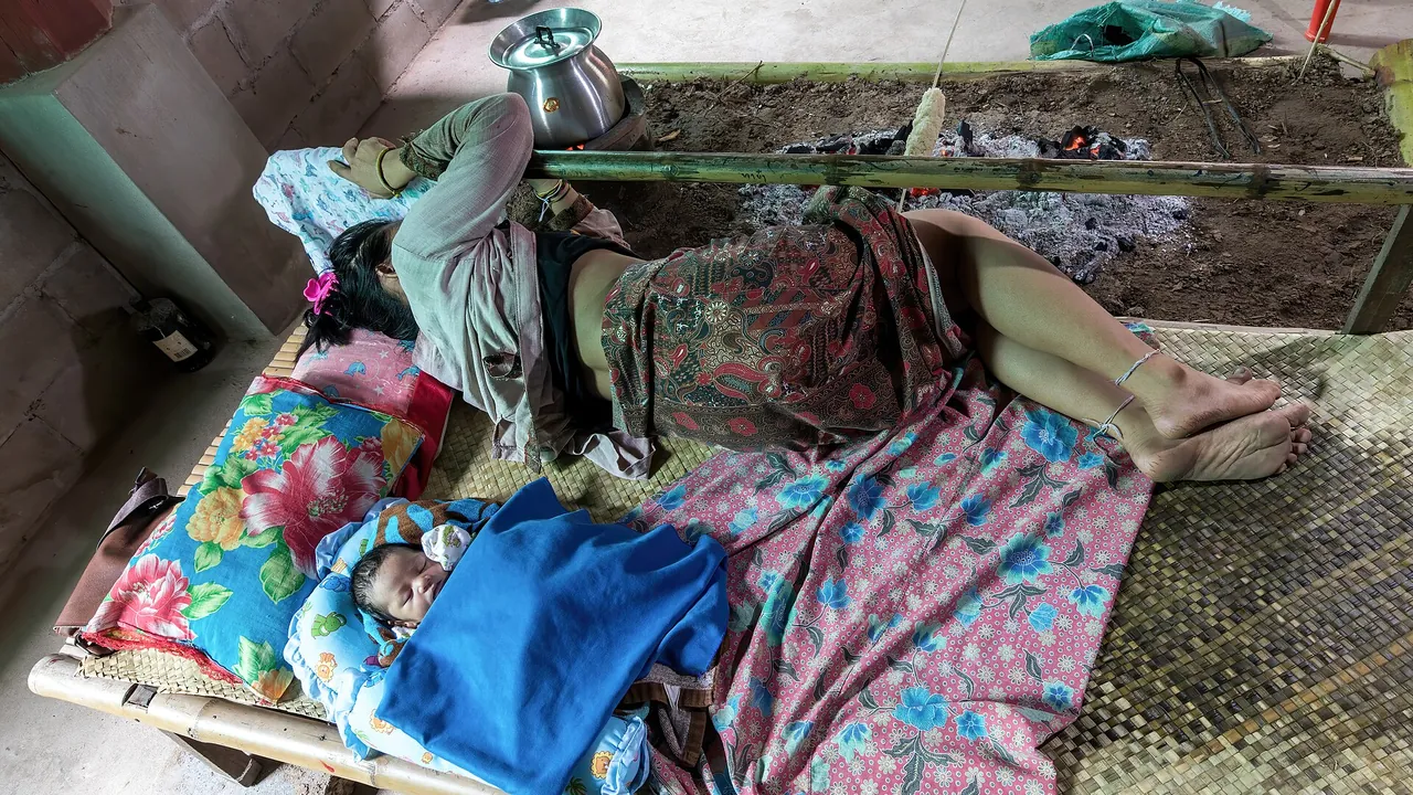 Mother and newborn sleeping on a bamboo bed near a campfire in a house in Don Det Laos