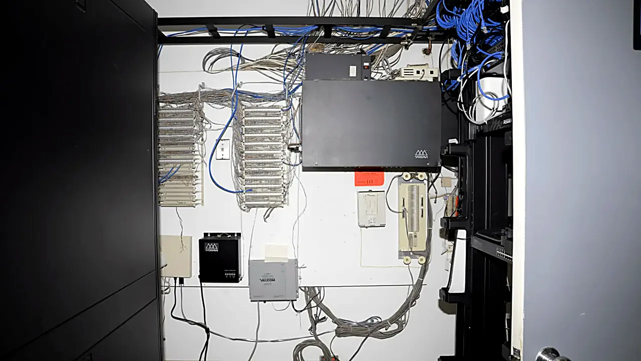EFTA00000440 - Cluttered server room with numerous cables equipment and racks arranged on a white wall