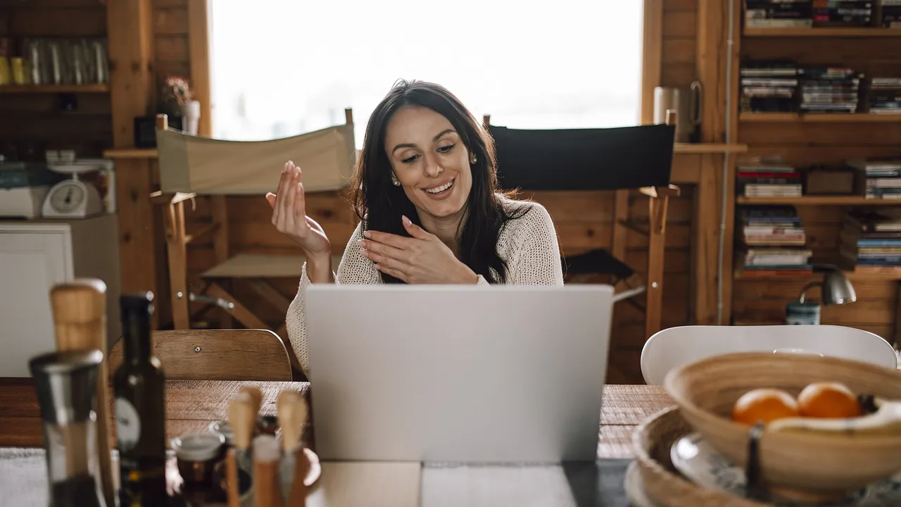 Woman smiling and using laptop during video call in cozy wooden room
